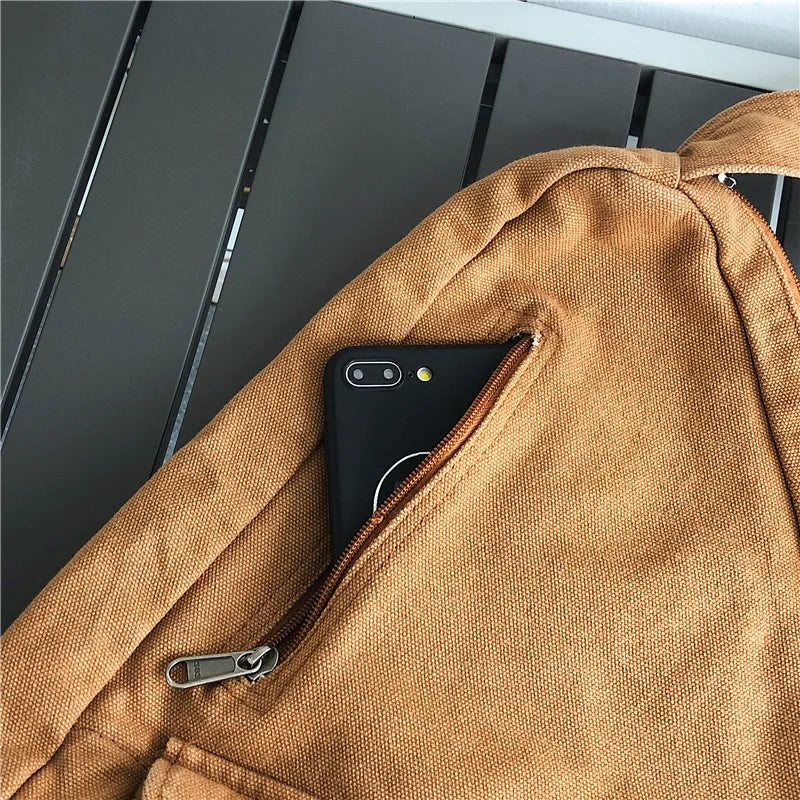 A tan canvas crossbody bag with a zippered pocket and a black smartphone visible inside.