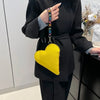 Cartera de monedas de forma de corazón amarilla y cuero PU con correa negra, sostenida por una persona con abrigo negro.