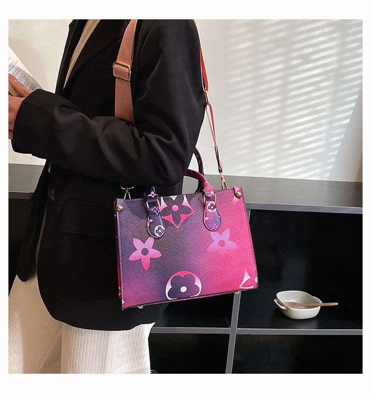 A woman holds a pink and purple patterned ladies' shoulder tote bag with a brown strap against a dark background.