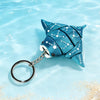 A teal 3D printed devil ray figurine with a silver chain attached, floating in clear blue water.