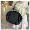 A woman wearing a cream knit sweater holds a black nylon shoulder bag with a patterned strap.