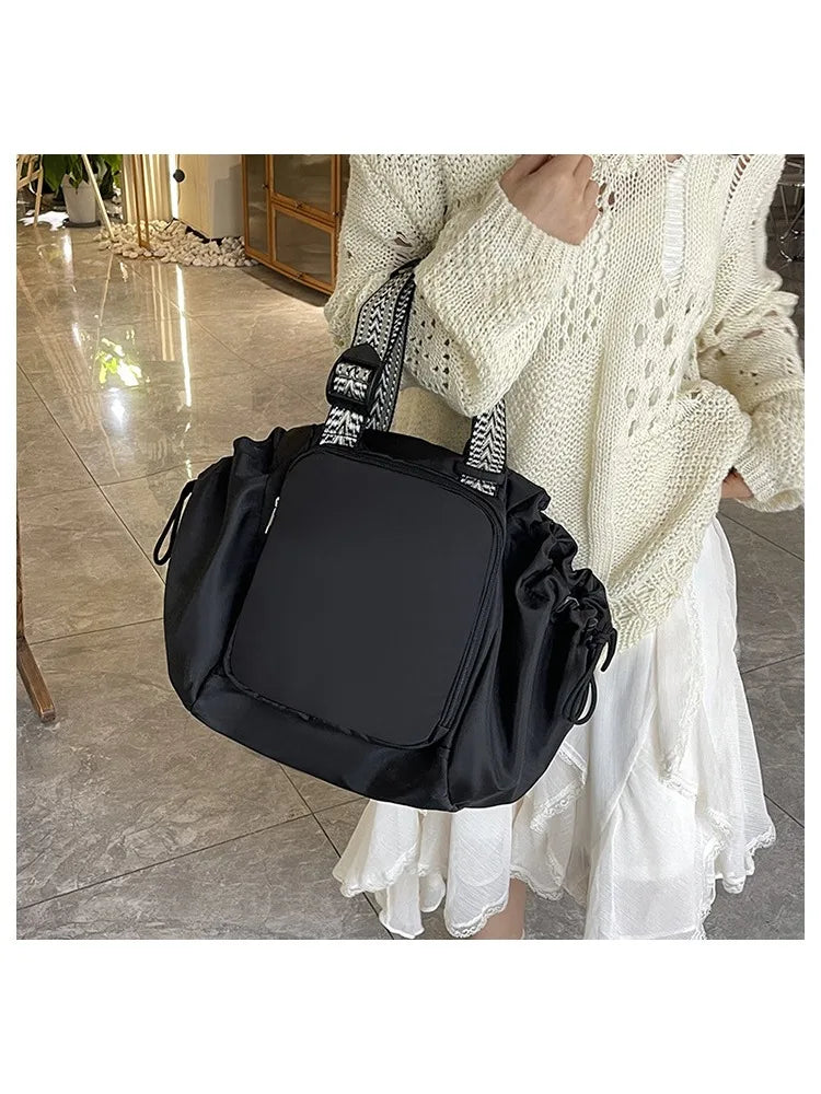 A woman wearing a cream knit sweater holds a black nylon shoulder bag with a patterned strap.