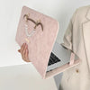 A pink slim PU laptop protective case with a gold-toned necklace charm is shown next to an open silver laptop.