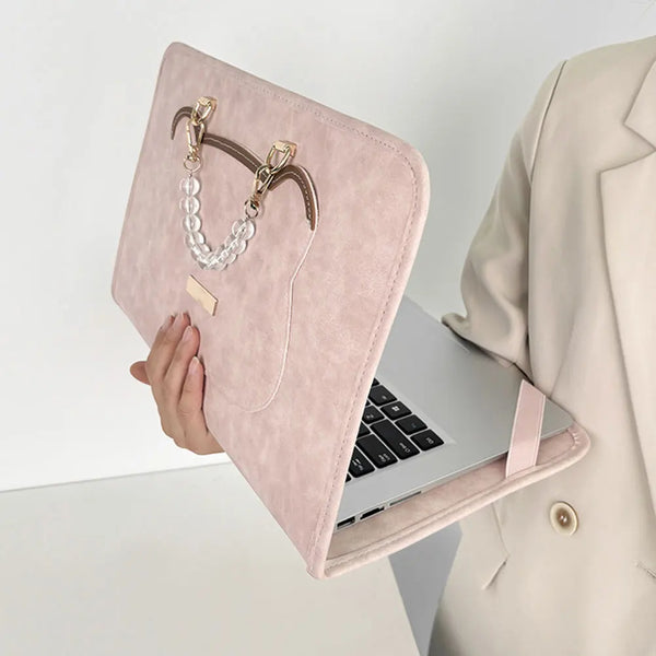 Une coque protectrice rose et mince en PU pour ordinateur portable avec un pendentif à la chaîne dorée est montrée à côté d'u