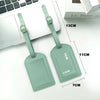 A pair of light green PU leather luggage tags with ID card holders shown next to a laptop.
