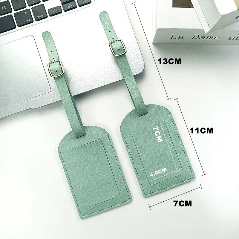 A pair of light green PU leather luggage tags with ID card holders shown next to a laptop.