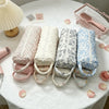 Five quilted storage bags in various floral patterns are displayed on a white table with a pink basket nearby.