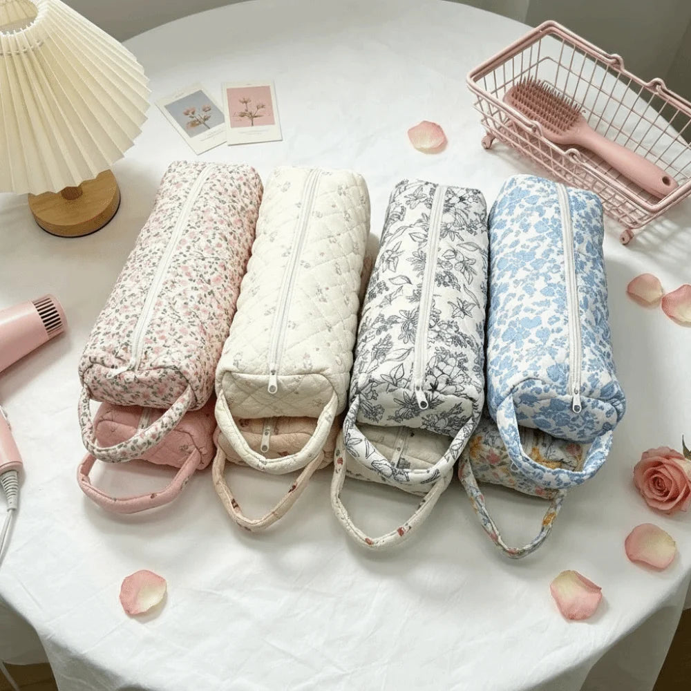 Five quilted storage bags in various floral patterns are displayed on a white table with a pink basket nearby.