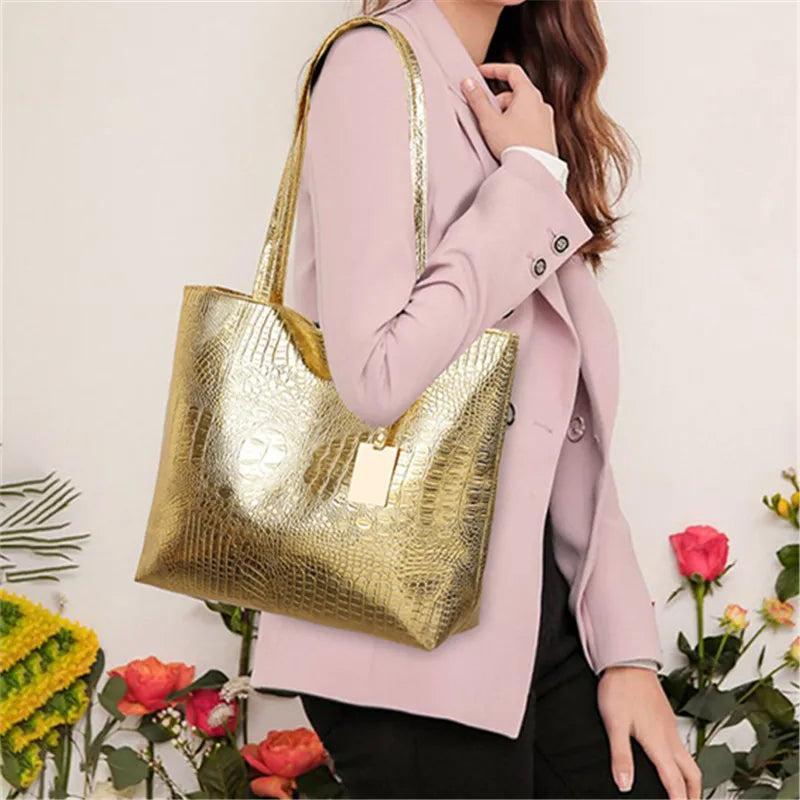 A woman holds a gold metallic zipper tote bag in front of a pink blazer.