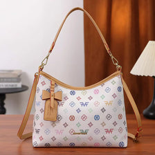 A beige leather crescent tote bag with a white and pink letter print and a brown bow accent resting on a wooden surface.