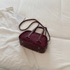 A deep burgundy retro crocodile textured mini crossbody bag resting on a white linen fabric.