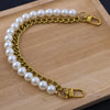 A gold-toned pearl chain shoulder strap is laid out on a wooden surface.