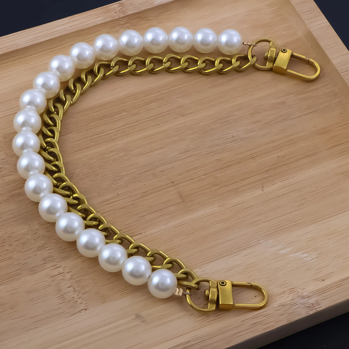 A gold-toned pearl chain shoulder strap is laid out on a wooden surface.