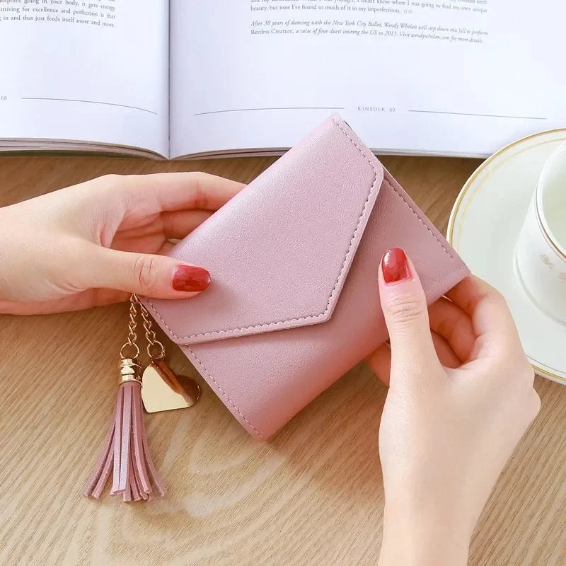 A hand holds a light pink waterproof nylon crossbody bag with a gold tassel on a wooden surface.