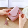 A hand holds a light pink waterproof nylon crossbody bag with a gold tassel on a wooden surface.