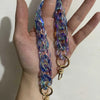 A hand holds a long, iridescent blue resin chain strap with a gold clasp.