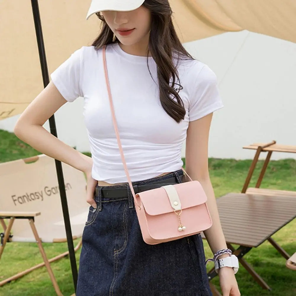 A woman wearing a white t-shirt and denim skirt holds a pink fashion square crossbody bag.
