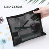 A black mesh cosmetic storage pouch with a drawstring closure is shown next to some flowers and paper.