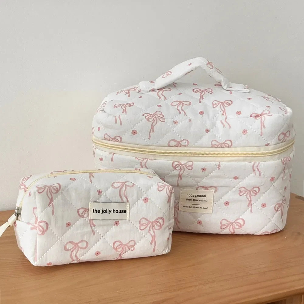 A white quilted cosmetic bag with pink ribbon details and a gold trim, shown in two views.