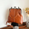 A brown leather shell handbag with a gold-toned strap is displayed against a white wall.