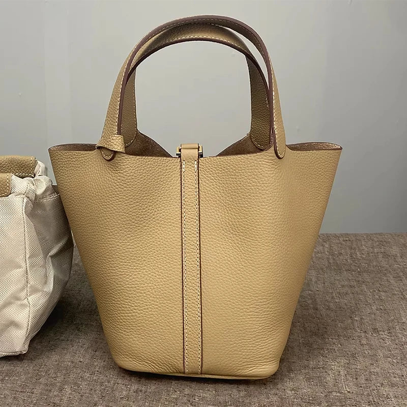 A beige classic genuine leather bucket bag with a light tan color is shown on a gray surface.