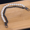 A silver-toned chain necklace featuring a strand of white pearls, laid out on a wooden cutting board.