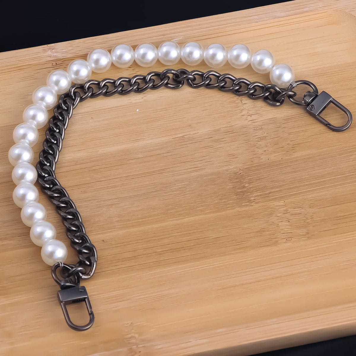 A silver-toned chain necklace featuring a strand of white pearls, laid out on a wooden cutting board.