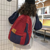 Back view of a red and navy canvas fashion backpack worn by a person in a modern indoor setting.