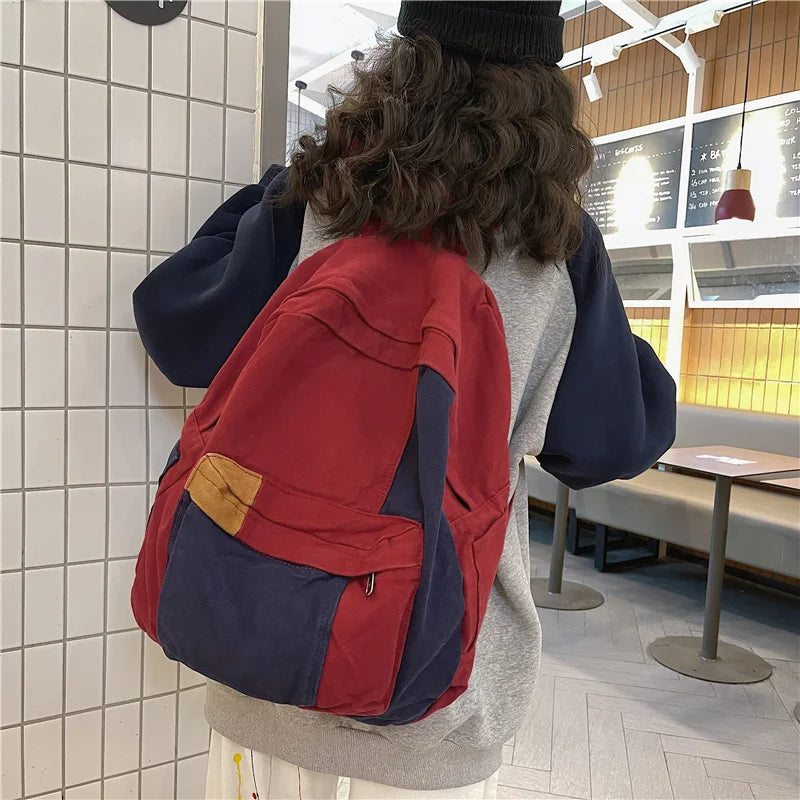 Back view of a red and navy canvas fashion backpack worn by a person in a modern indoor setting.