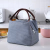 A navy blue and white striped thermal lunch bag with brown handles resting on a white surface.