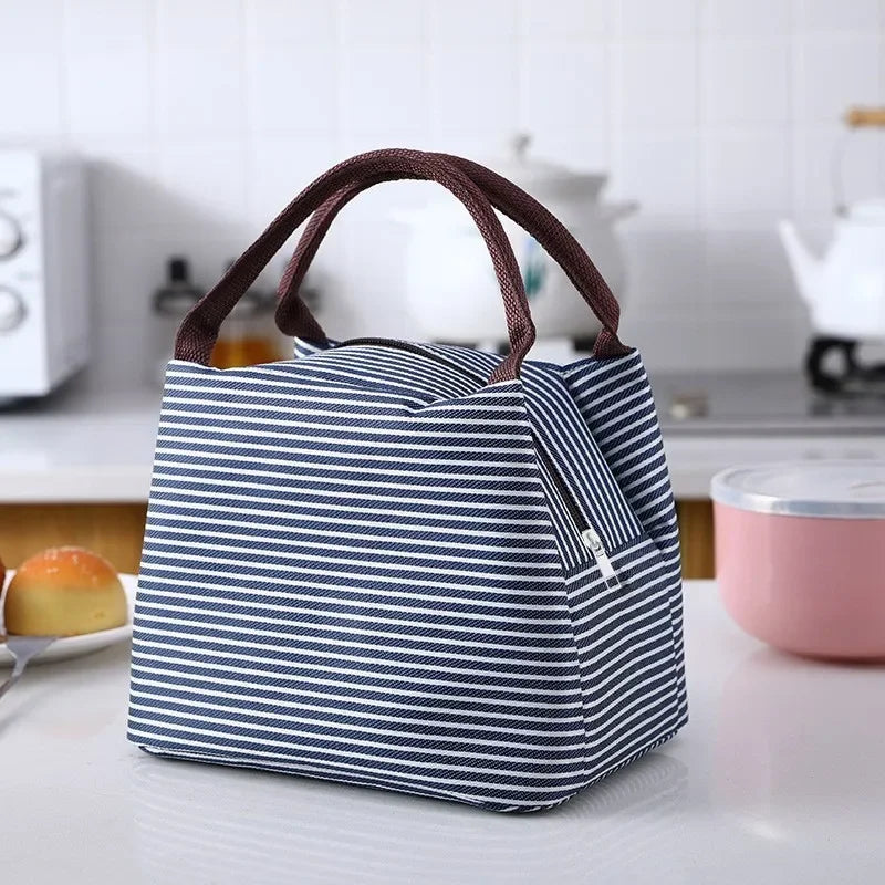 A navy blue and white striped thermal lunch bag with brown handles resting on a white surface.
