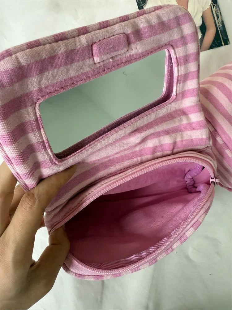 A pink striped makeup bag with a flip-top mirror is shown being held open.