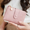 A hand holds a pink minimalist card holder wallet with gold accents against a light background.