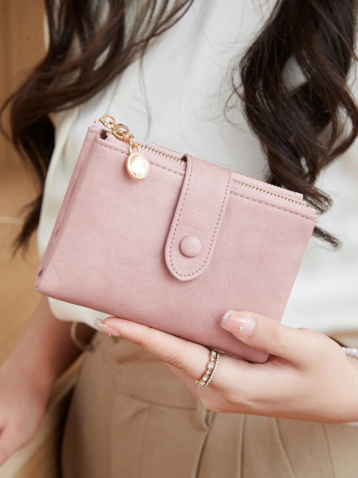 A hand holds a pink minimalist card holder wallet with gold accents against a light background.