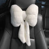 A white, fluffy bowknot car headrest pillow with lumbar support placed on a black leather seat.