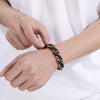 A hand is wearing a chunky black and gold Cuban link bracelet on the wrist.