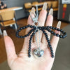 A hand holds a black beaded Y2K bowknot pearl keychain with a silver charm.
