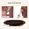 Nahaufnahme einer braunen Krokodilmuster-Top-Handtasche mit Crossbody-Gurt und goldfarbener Clipsverzierung.