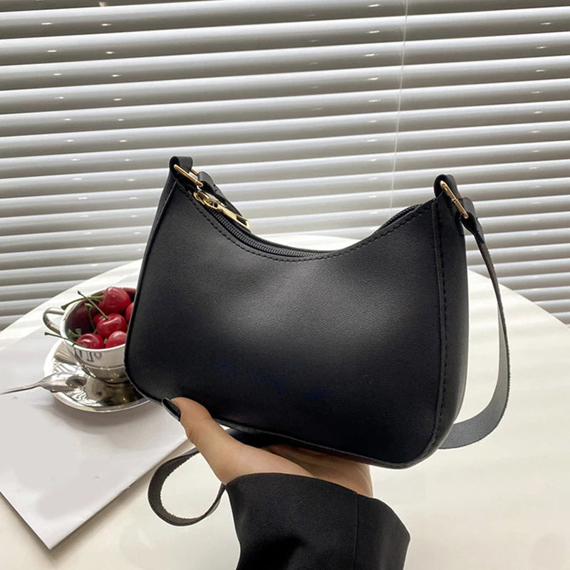 A black retro solid color PU leather shoulder bag with a gold-toned zipper and strap resting on a white surface.