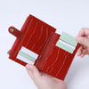 A hand holds a red leather card holder with a crocodile pattern and a zipper, displaying several cards.