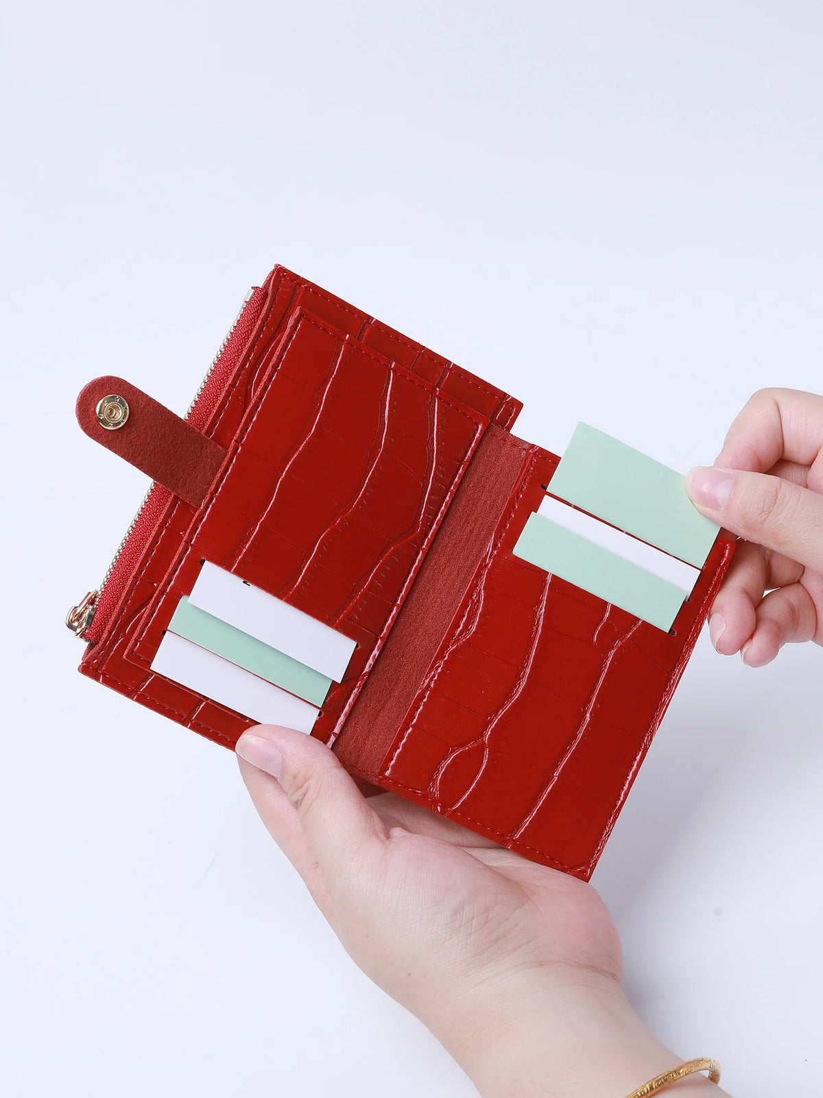 A hand holds a red leather card holder with a crocodile pattern and a zipper, displaying several cards.
