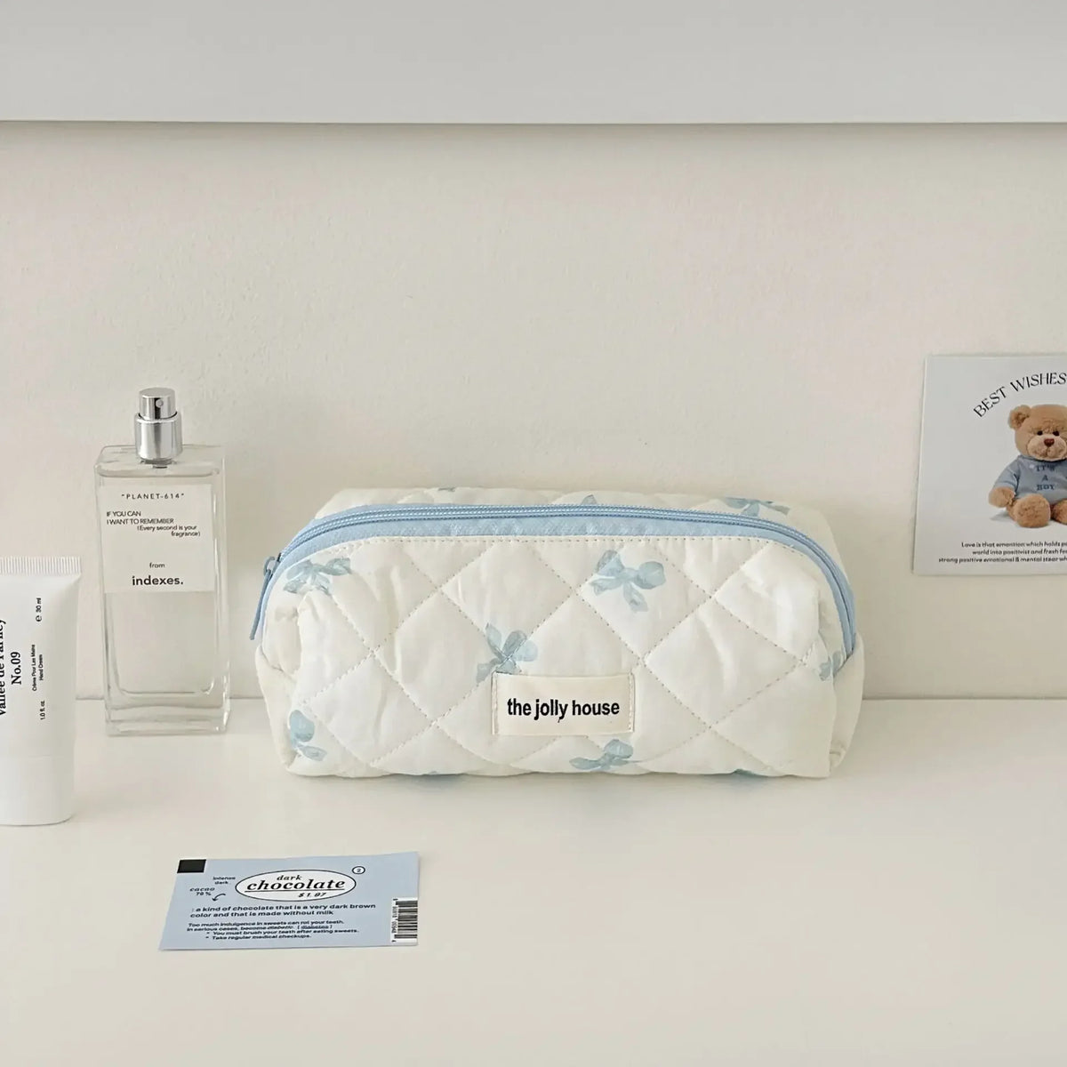 Sac de rangement cosmétique rembourré blanc avec accents bleus, étiqueté The Jolly House, posé sur une surface claire.