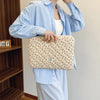 Una mujer con una camisa azul claro sostiene una funda acolchada para portátil con estampado de flores beige.