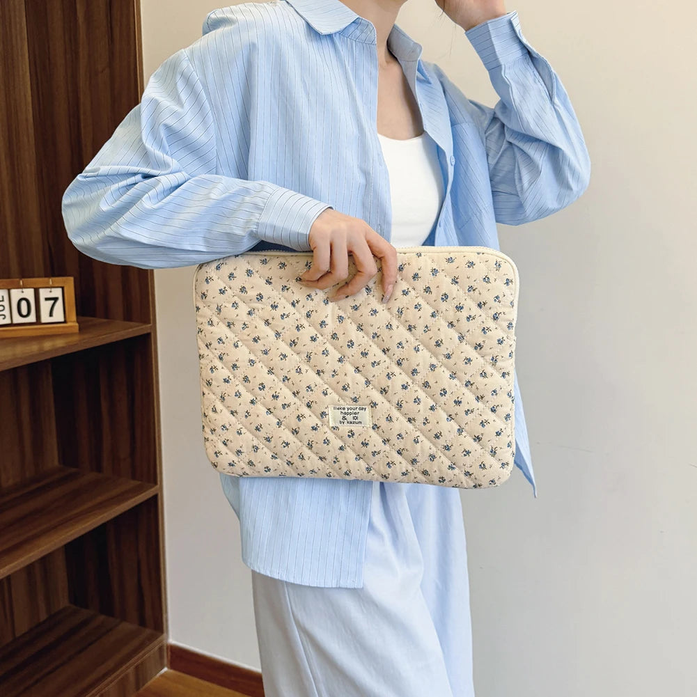 Una mujer con una camisa azul claro sostiene una funda acolchada para portátil con estampado de flores beige.