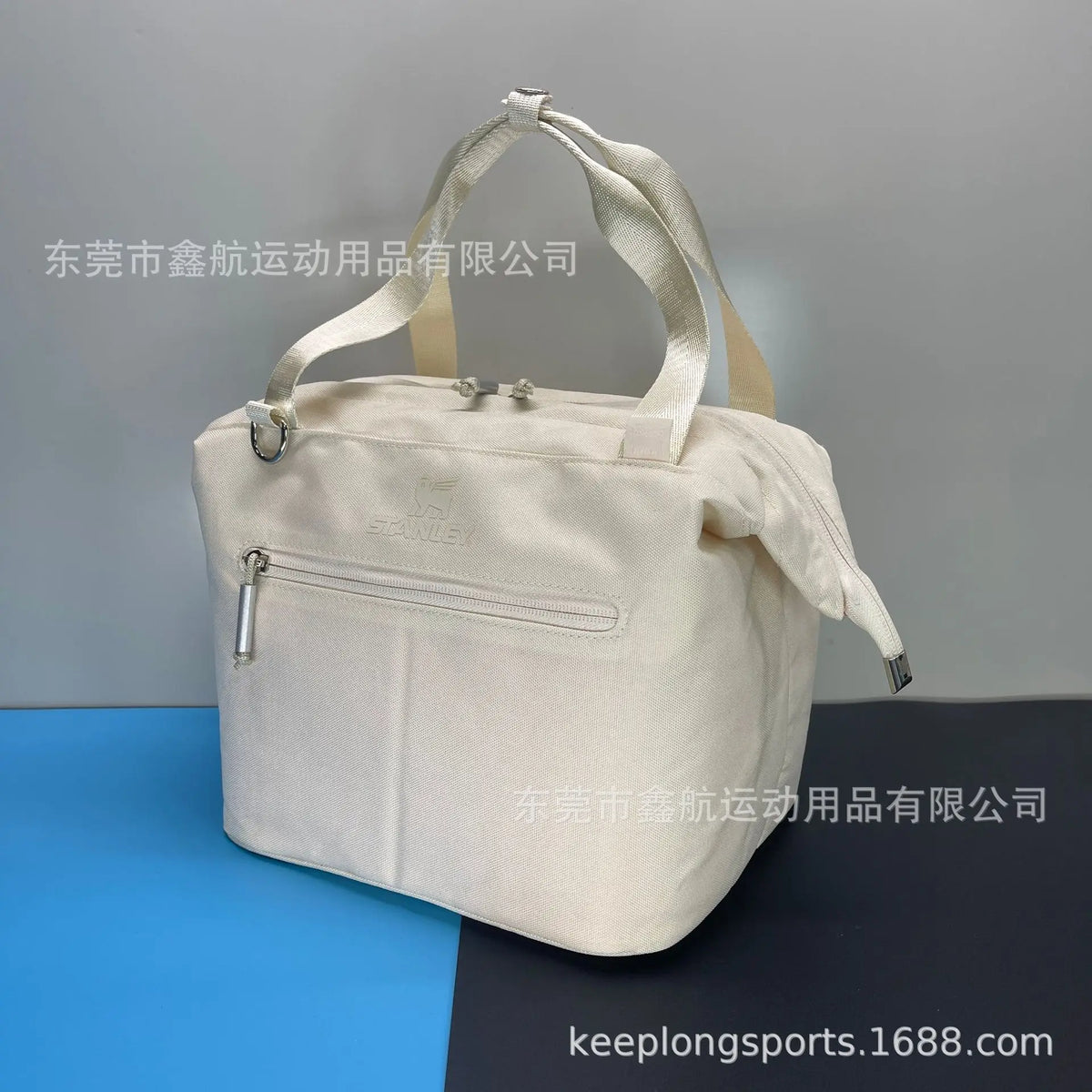 A cream-colored insulated cooler lunch bag with a detachable strap is shown against a dark background.