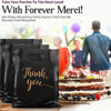 Black thank you gift bags with gold lettering displayed on a wooden surface.