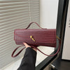 A hand holds a burgundy crocodile-embossed PU leather clutch bag with a gold clasp against a light background.