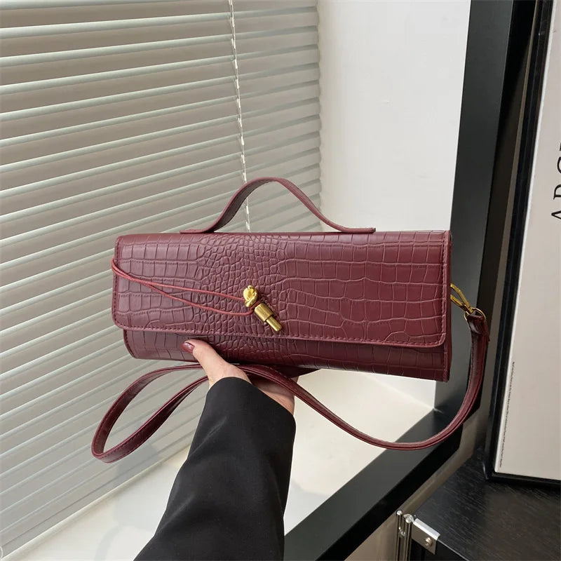 A hand holds a burgundy crocodile-embossed PU leather clutch bag with a gold clasp against a light background.