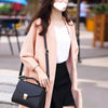 A woman wearing a pink coat and black skirt holds a black leather crossbody bag.