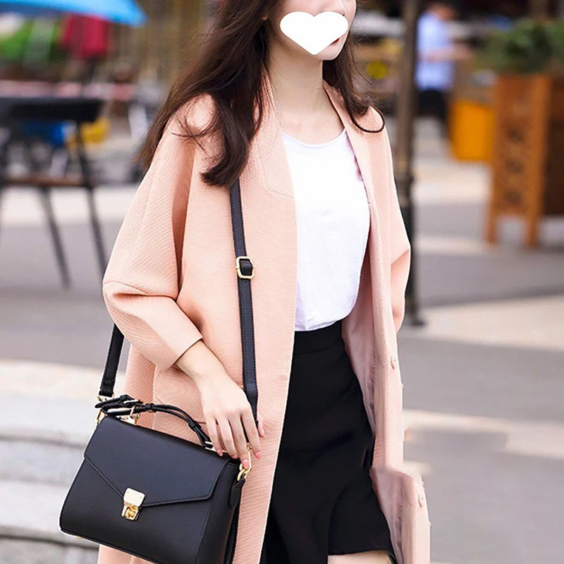 A woman wearing a pink coat and black skirt holds a black leather crossbody bag.